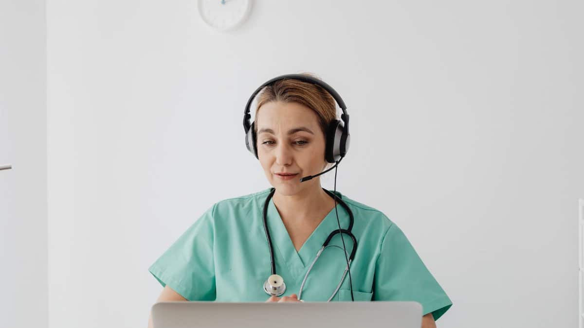 A female doctor in scrubs using a laptop for a virtual consultation, enhancing telemedicine.