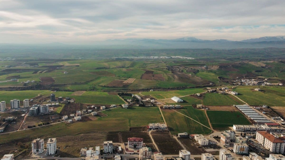 Stunning aerial view of city buildings meeting expansive countryside fields under a cloudy sky.