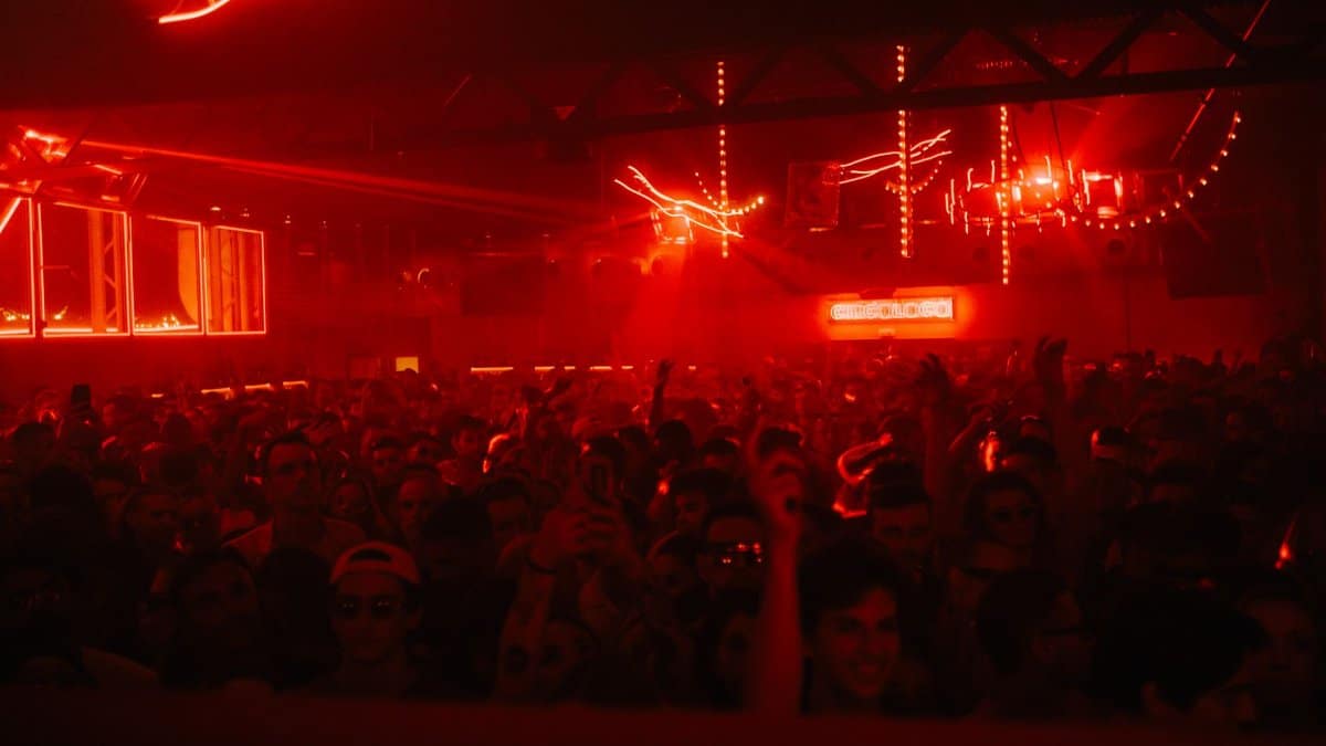 A packed nightclub with a vibrant atmosphere, red lights, and dancing crowd.