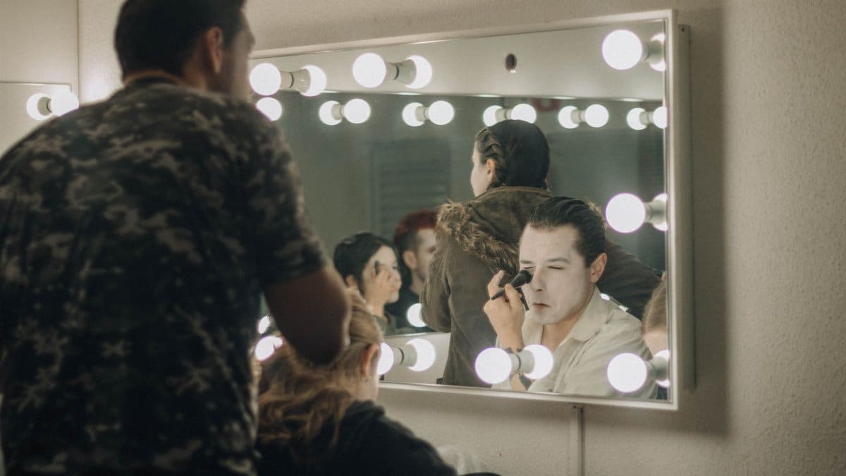 Actors applying makeup backstage in illuminated dressing room before a performance.