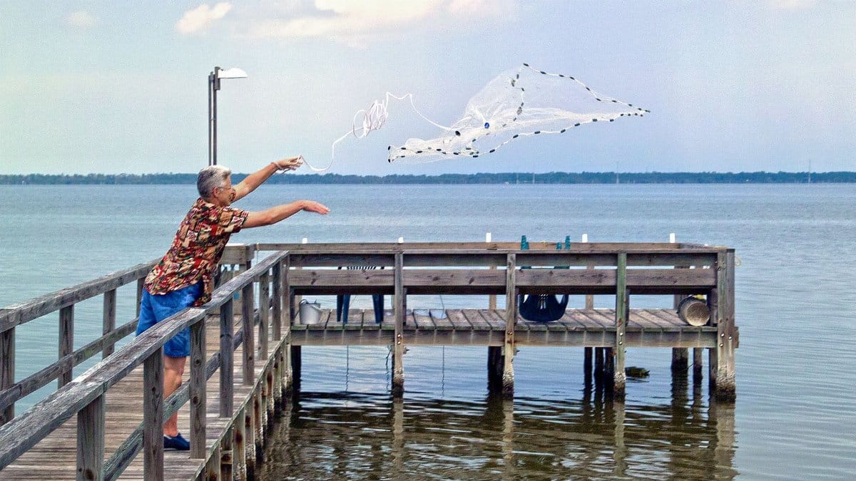 A man casting a net from a dock into a serene lake in Florida, showcasing traditional fishing techniques.
