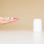 Side view of crop unrecognizable person with palm full of double colored pills near table with white plastic jar
