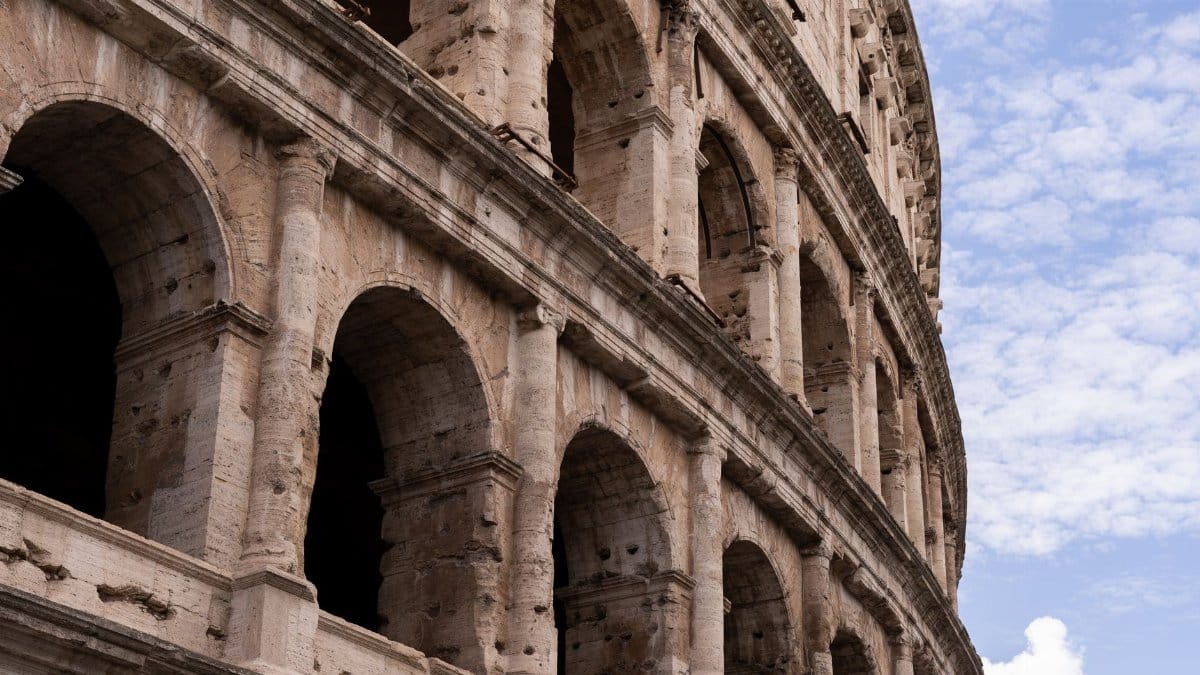 Detailed view of the Colosseum in Rome, showcasing its historic arches and stone texture against a blue sky.