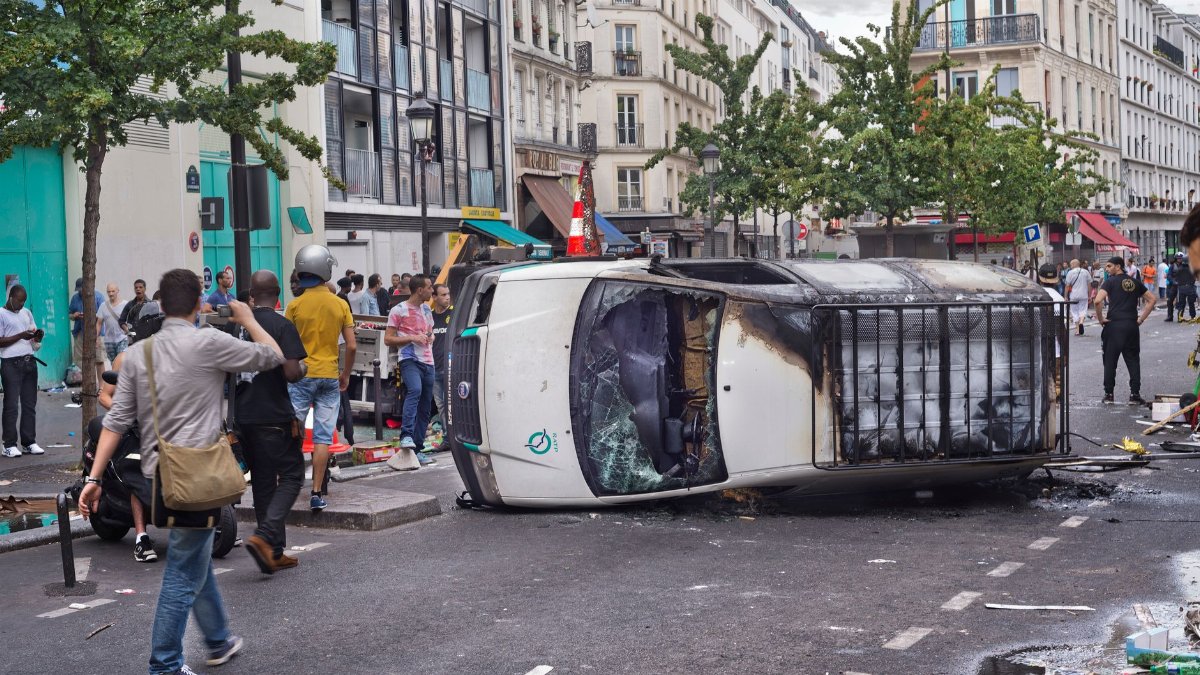 A busy city street with an overturned vehicle and gathered crowd capturing the moment.