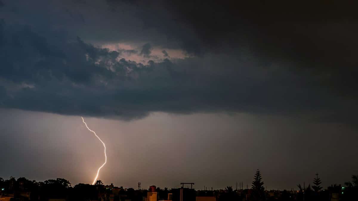 A powerful lightning strike illuminates the cityscape under dark storm clouds, showcasing nature's raw power at night.