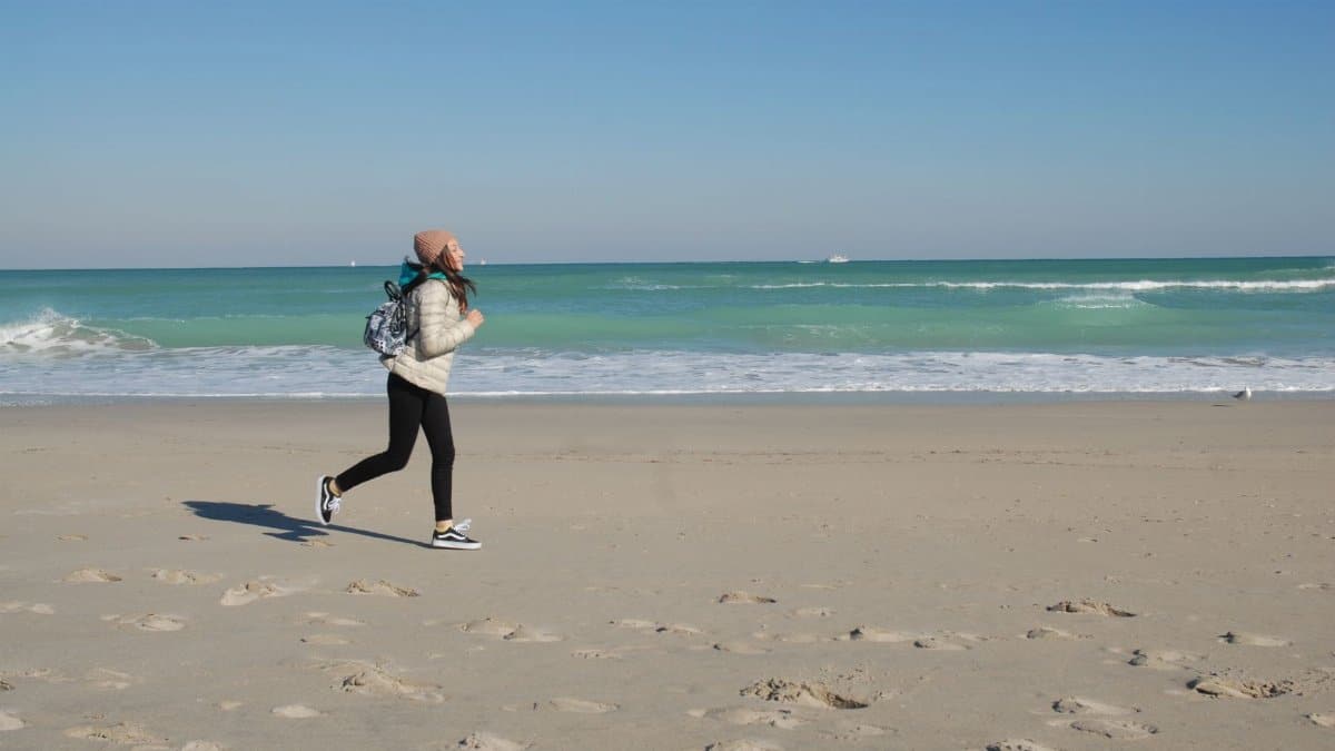 Active woman jogging on a sunny Miami beach with clear skies and turquoise waters.
