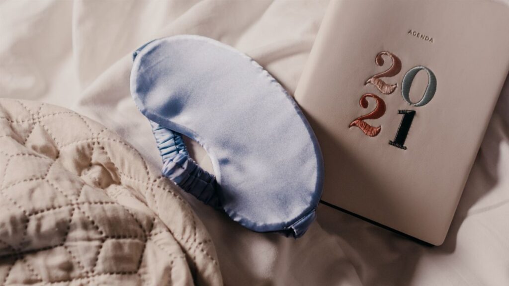 A soft blue sleep mask and 2021 planner on a quilted bedspread create a serene setting.