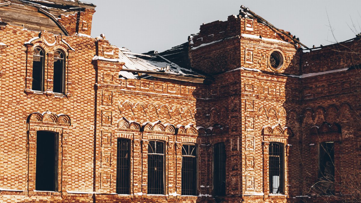 Sunlit view of a damaged historic brick building with ornate architecture.