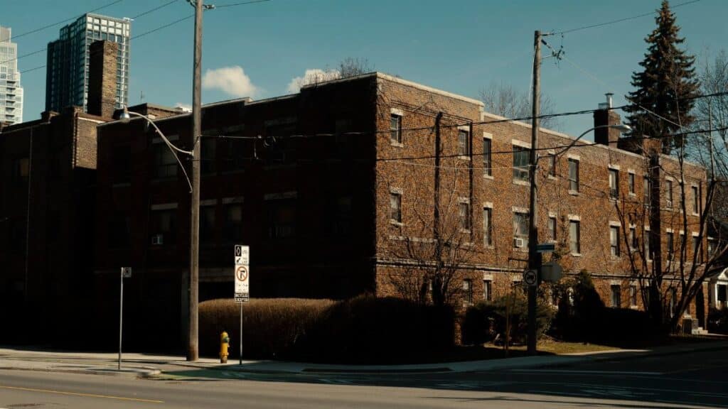 Street view of brick apartment building with blue sky and modern backdrop.