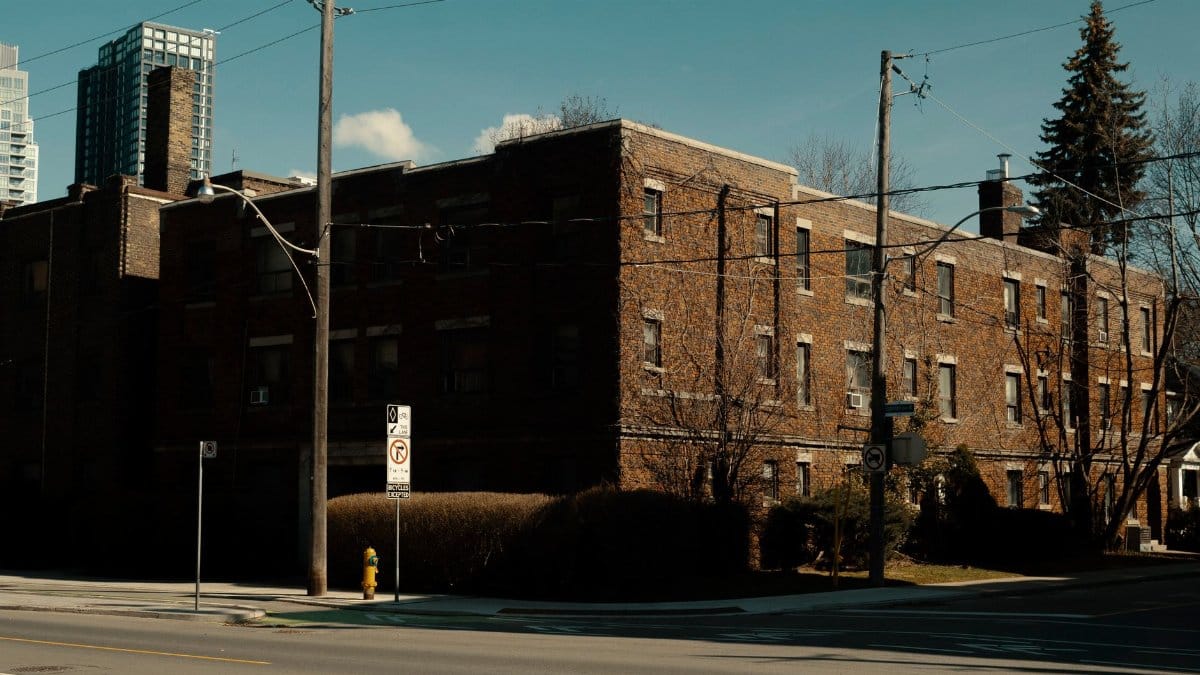 Street view of brick apartment building with blue sky and modern backdrop.