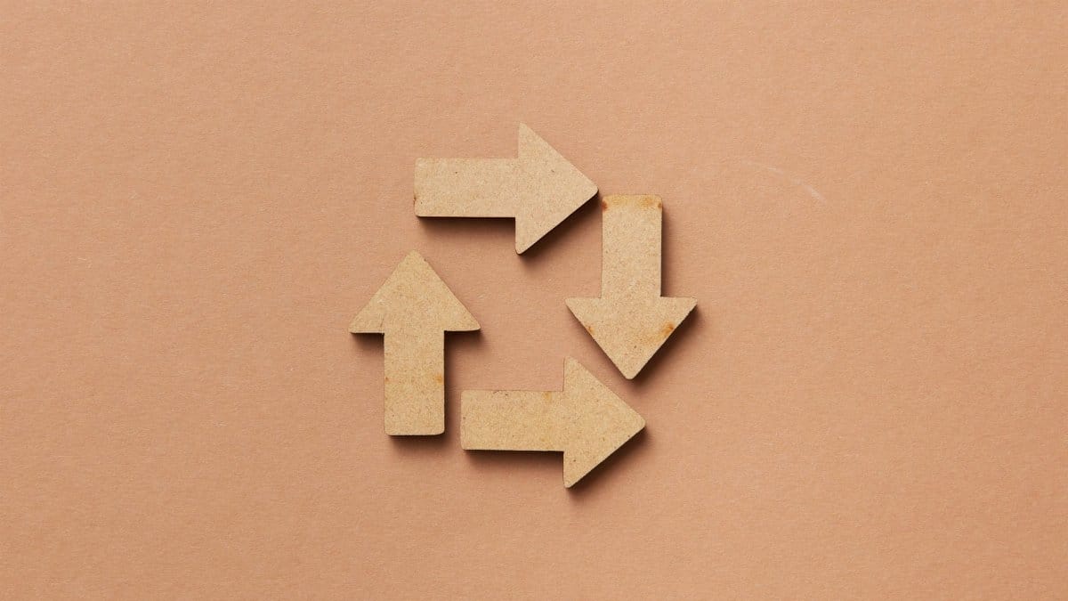 Close-up of a recycling symbol made from wooden arrows on a beige background.