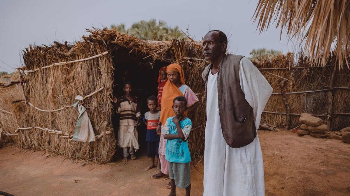 Portrait of family standing outside a traditional straw hut in a rural village.