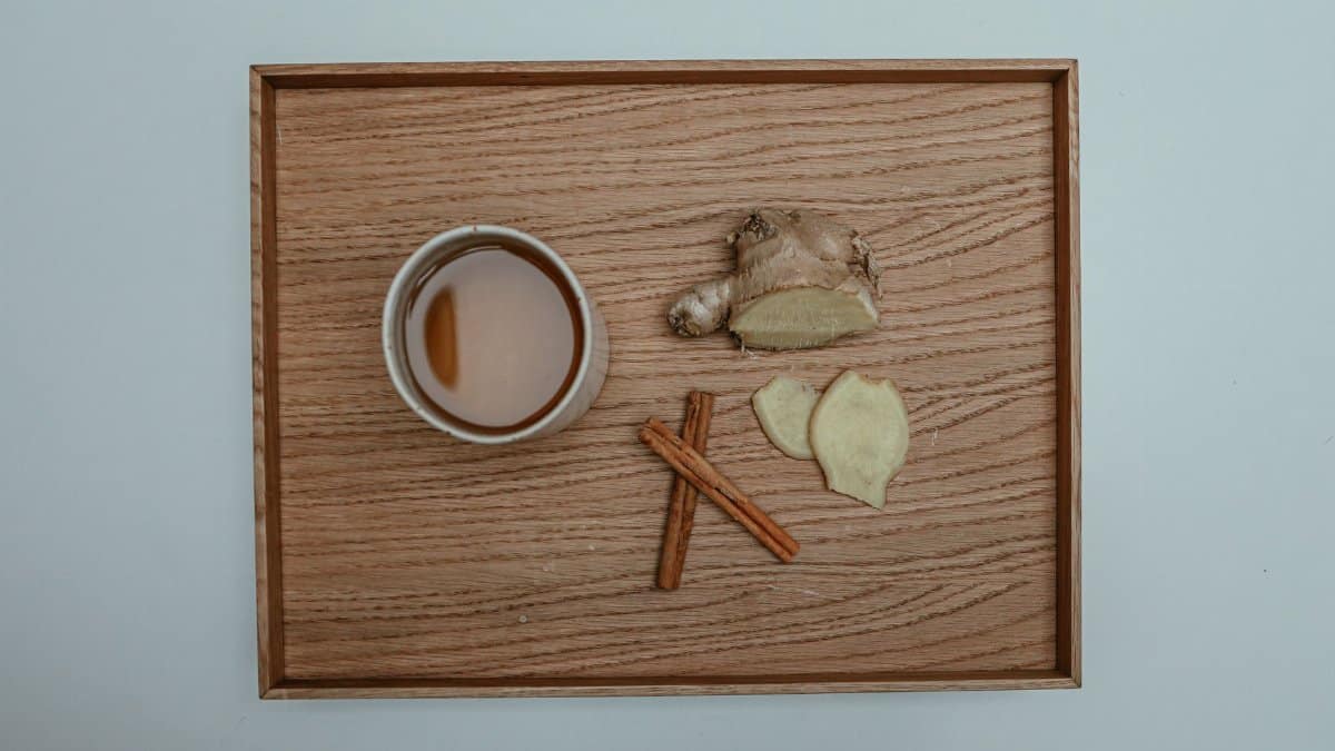 Flat lay image of a cup of tea with cinnamon sticks and fresh ginger on a wooden tray.