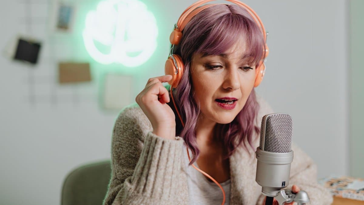 A woman recording a podcast indoors with headphones and a microphone.
