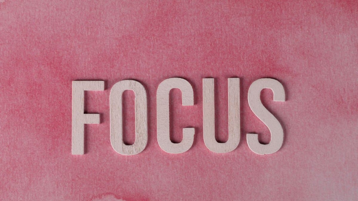 Close-up of 'FOCUS' in wooden letters on a pink textured background.