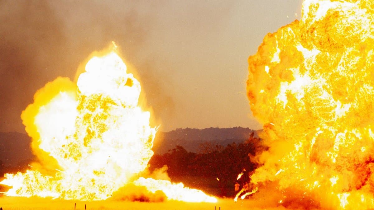 Powerful explosion with bright flames against an outdoor landscape, creating a dramatic visual impact.
