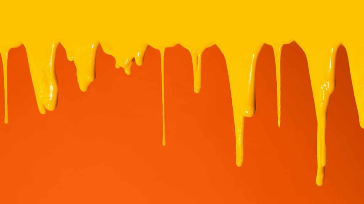 Abstract image of vivid yellow paint drips against an orange backdrop.