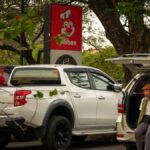 A man in an open car trunk at Manila parking lot with Jollibee sign nearby.