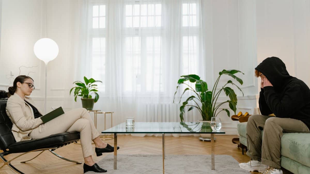 A therapist listens to a patient in a comfortable office setting. The atmosphere is calm and professional.