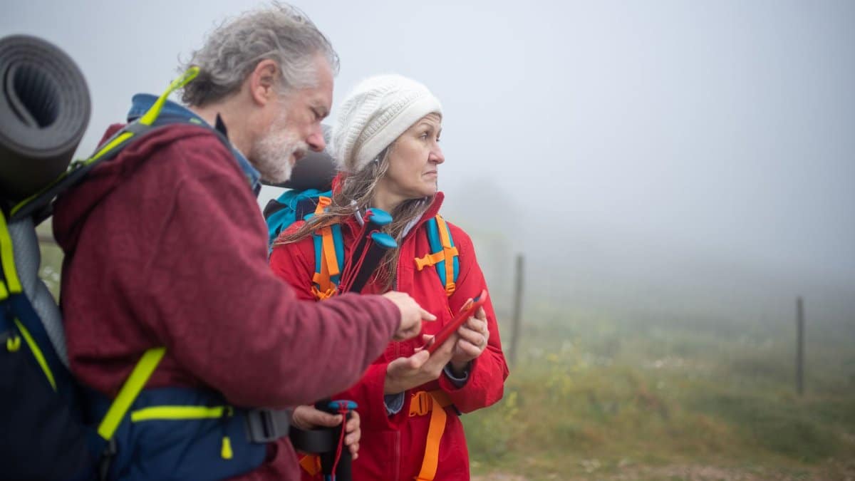 Two hikers consult a smartphone in a foggy rural landscape in Portugal.