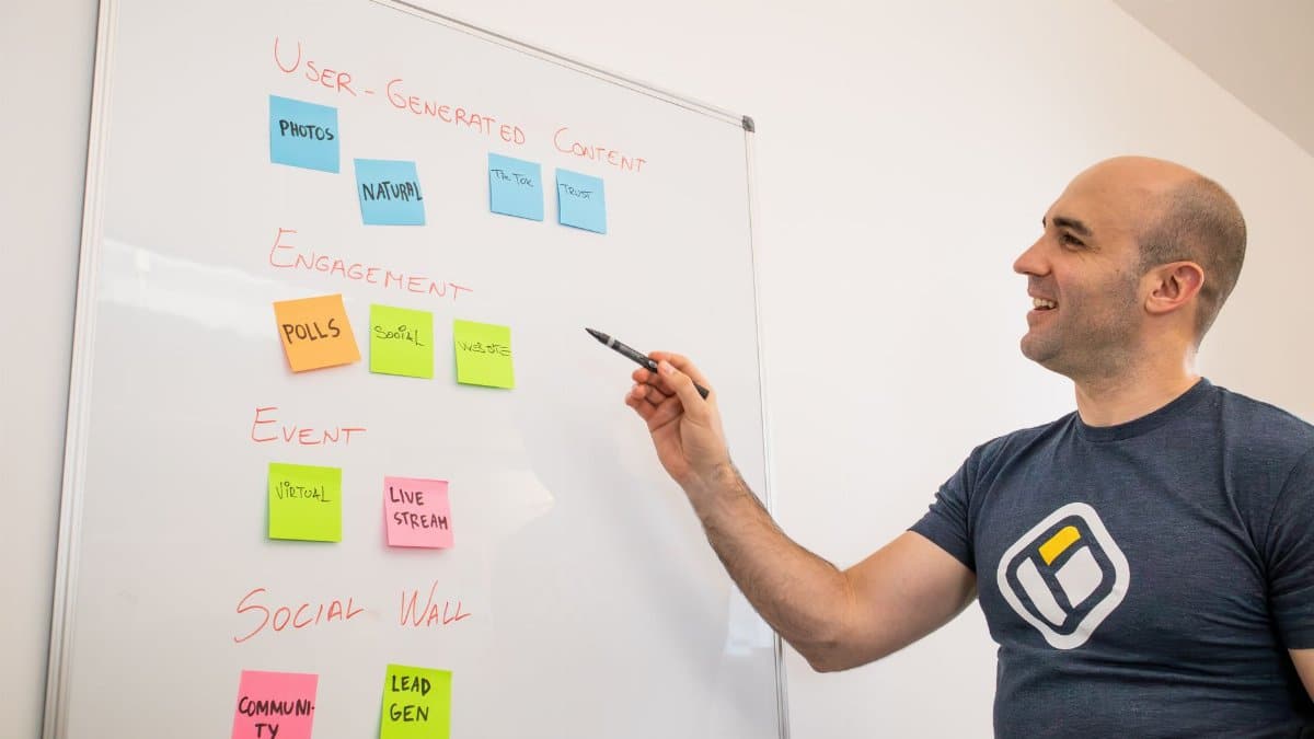 Smiling man presents strategies on a whiteboard with post-its, focusing on engagement and user-generated content.