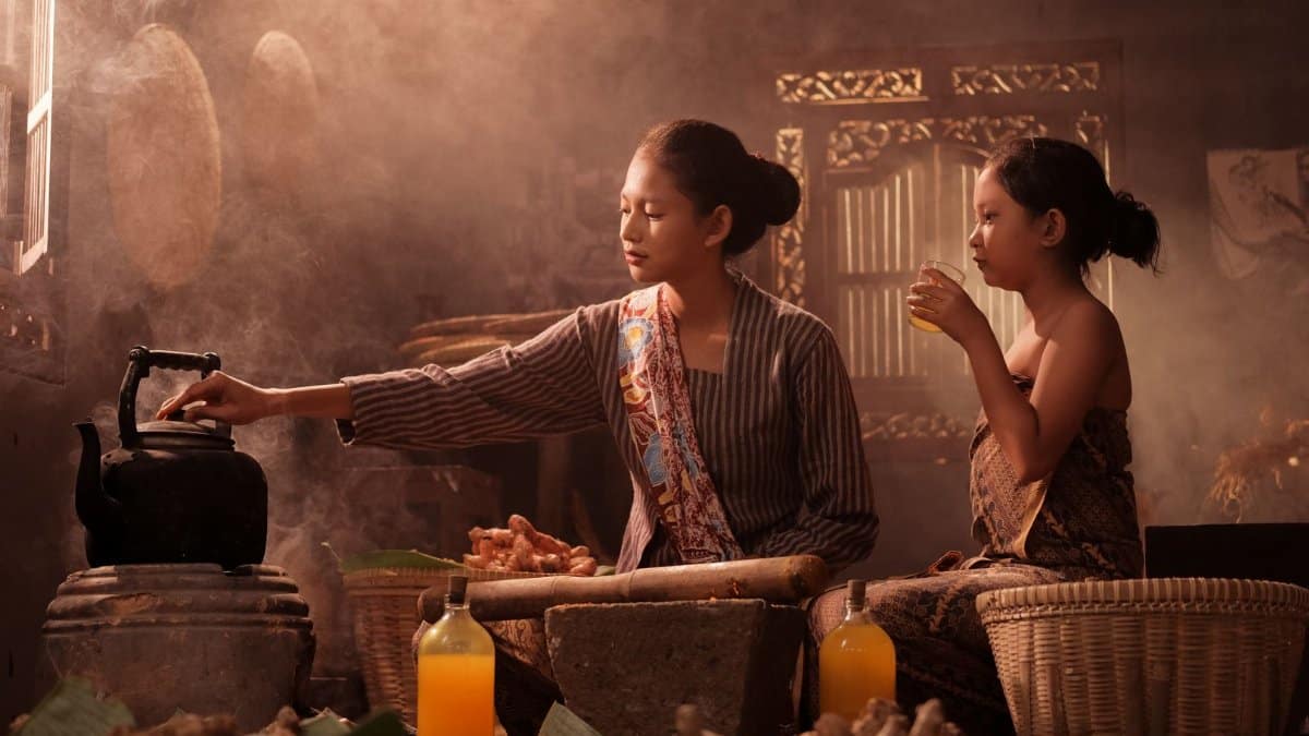 Mother and daughter in traditional Indonesian kitchen, cooking and drinking.