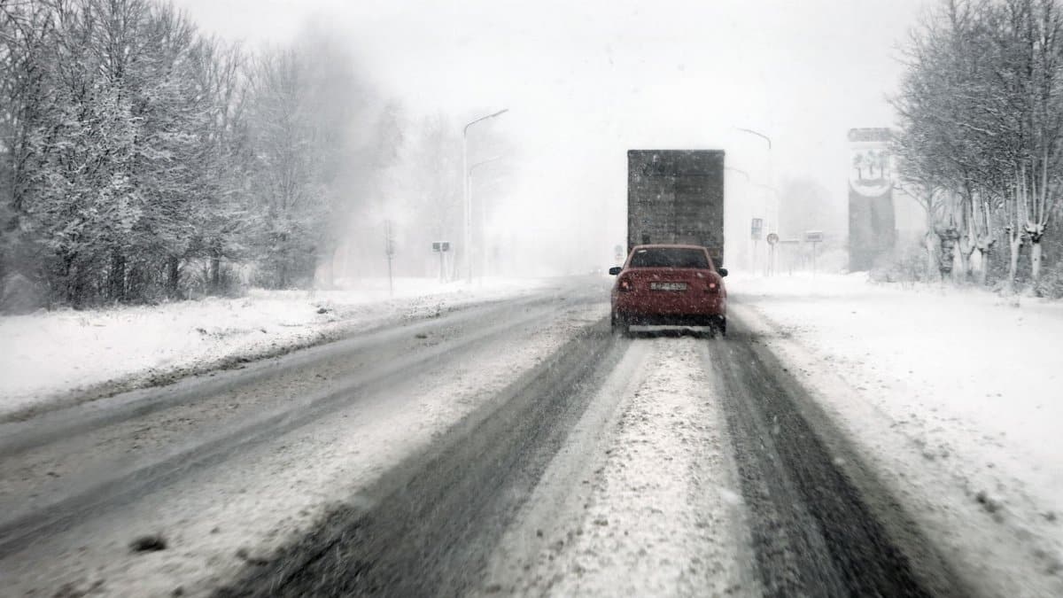 Cars navigate a snowy highway during a blizzard, showcasing tough winter driving conditions.