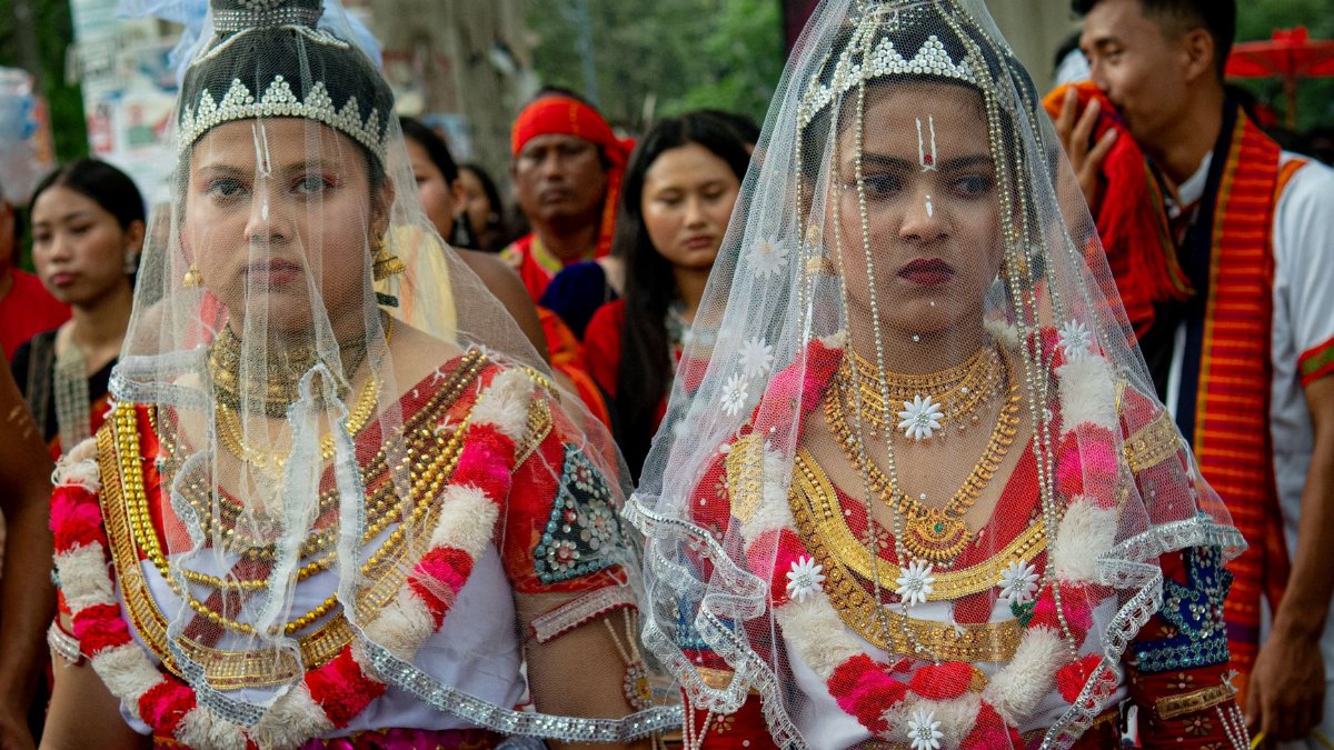 Two women in vibrant traditional attire participate in a cultural parade, showcasing elaborate jewelry and headpieces.