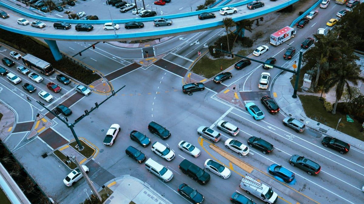 Aerial view of a busy urban intersection filled with cars and traffic under a blue overpass.