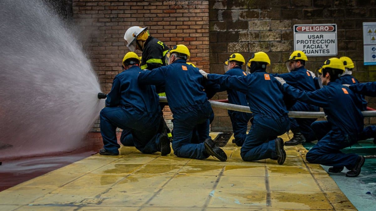 Group of firefighters in training, using a water hose during a practice drill, emphasizing teamwork and safety.