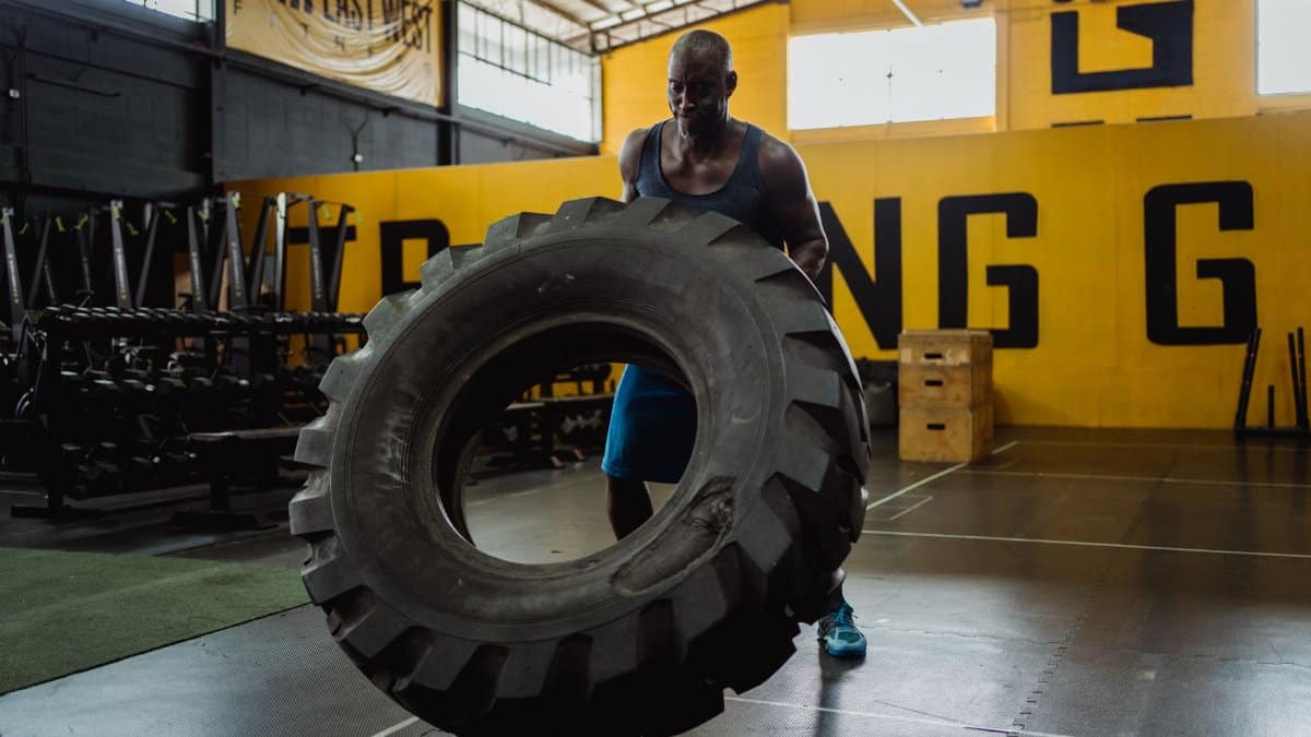 Muscular man exercising with large tire for strength training in a gym.