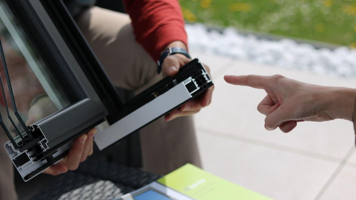 Close-up of two people examining an aluminum window frame outdoors.