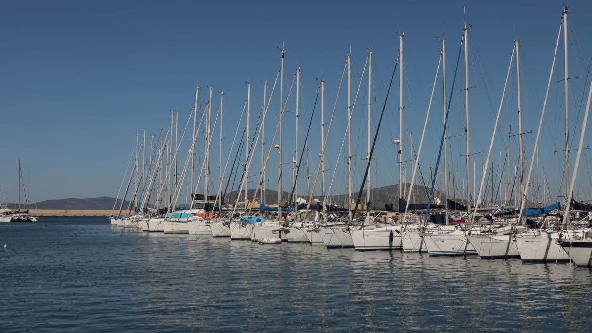 A tranquil marina with yachts moored in a row under a clear blue sky, perfect for travel enthusiasts.