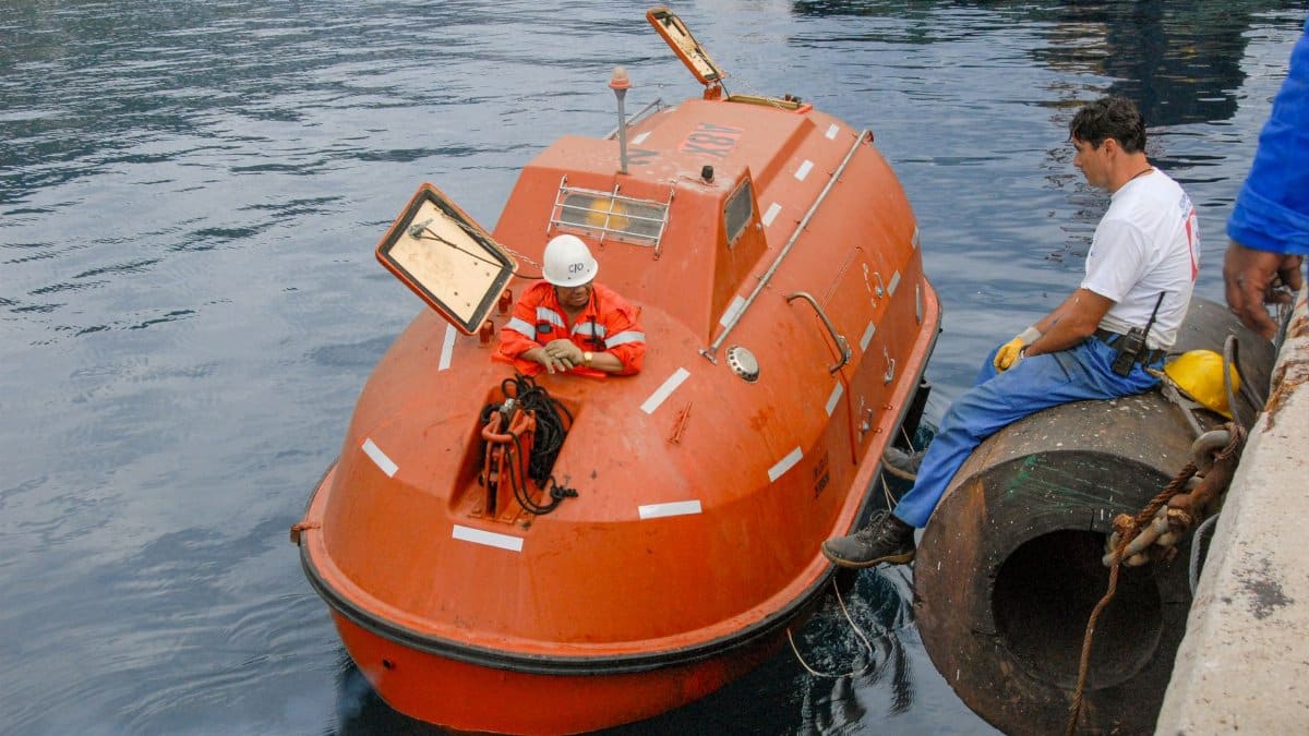 Crew members prepare a lifeboat for launch at a harbor. Maritime safety equipment and procedures.