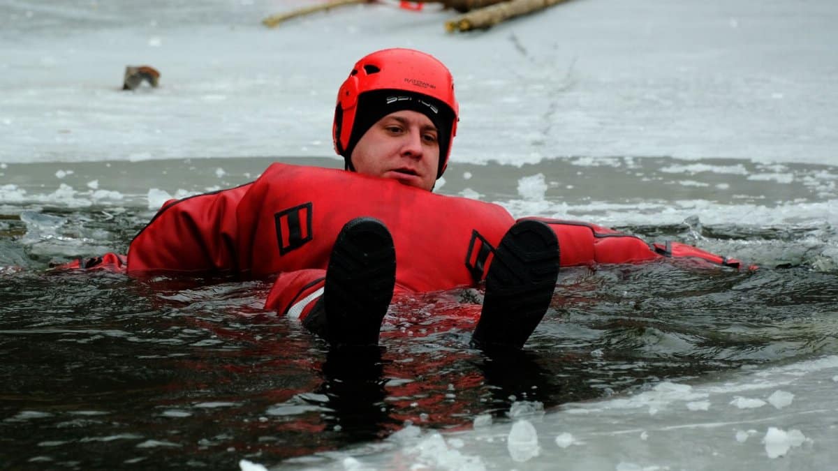 Person practicing ice rescue in a red suit on a frozen lake during winter training.