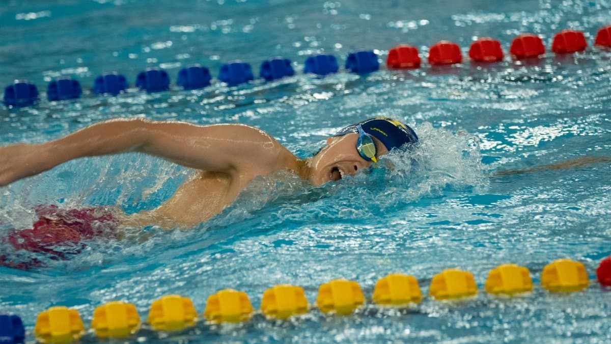 Swimmer performing freestyle stroke in an indoor pool during competition.