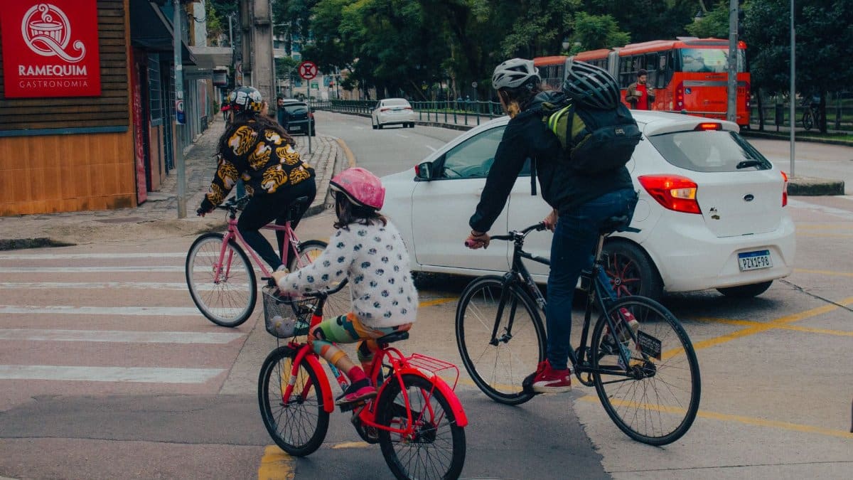 A family biking through a city intersection on a cloudy day, wearing helmets for safety.