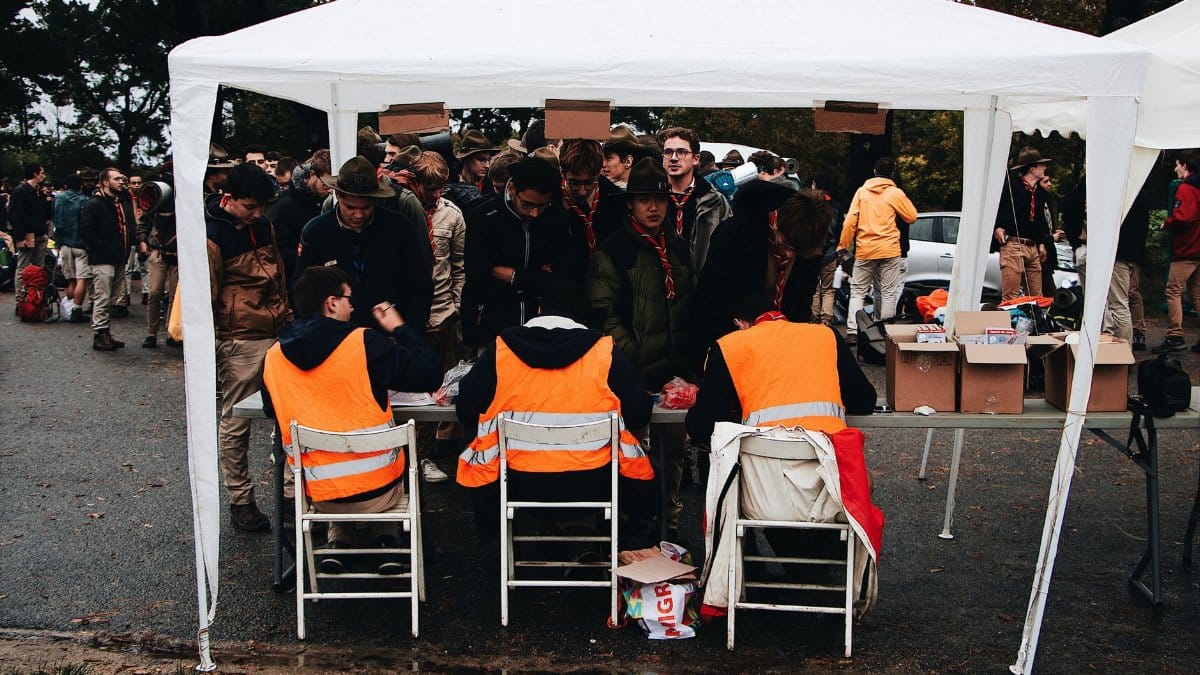 Crowded outdoor check-in tent at an event with attendees in fluorescent vests and scout uniforms.