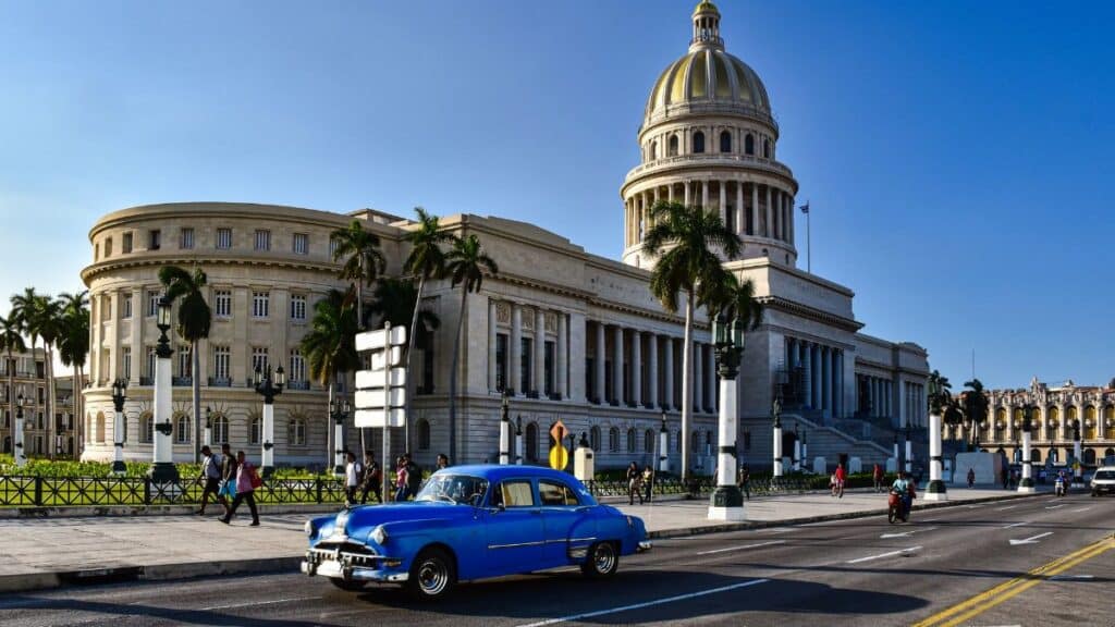 Classic blue car on Havana street with iconic Capitolio building in background.