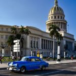 Classic blue car on Havana street with iconic Capitolio building in background.