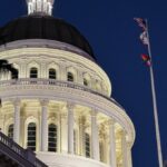 Illuminated California State Capitol dome with flags at dusk, Sacramento, USA.