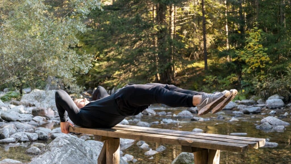 Man performing a core exercise on a bench by a serene river in a forest setting.