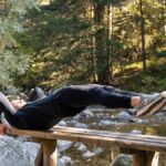 Man performing a core exercise on a bench by a serene river in a forest setting.