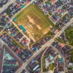 Drone shot of a vibrant neighborhood with a central football field, showcasing urban planning.