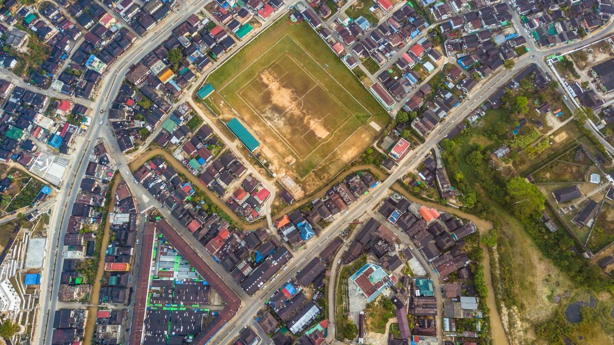 Drone shot of a vibrant neighborhood with a central football field, showcasing urban planning.