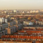 Aerial view of a cityscape featuring dense residential housing under a warm sunset glow.