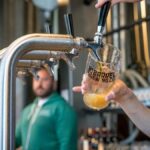 Close-up of beer being poured at a modern brewery taproom with bartender in background.