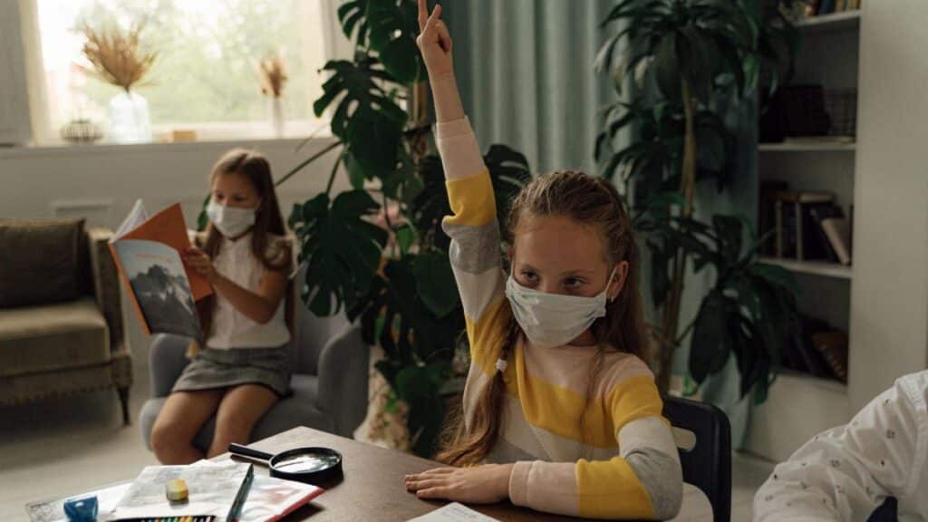 Children studying indoors while wearing facemasks for health safety measures.