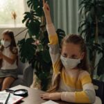 Children studying indoors while wearing facemasks for health safety measures.