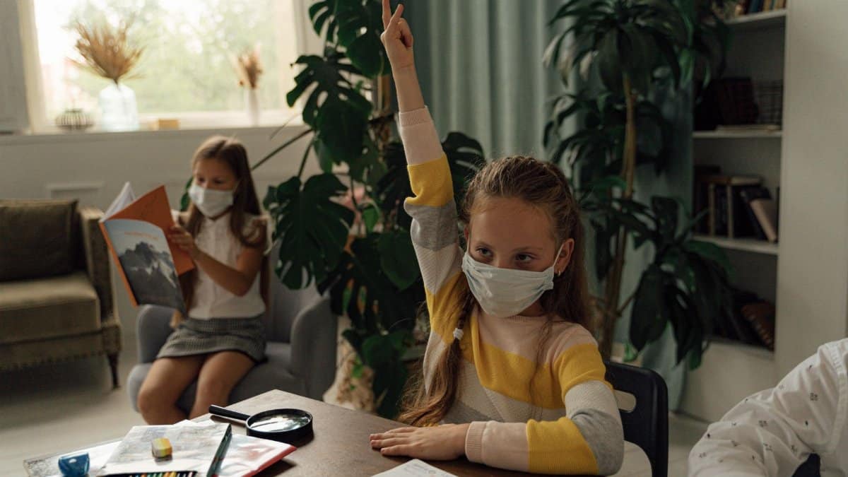 Children studying indoors while wearing facemasks for health safety measures.